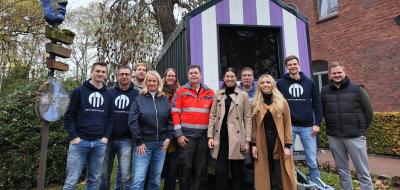 Personengruppe vor einem kleinen Holzhaus