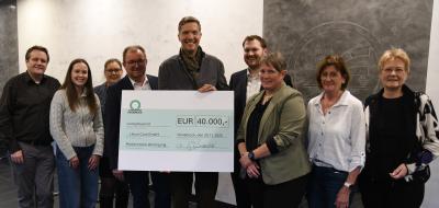 Eine Personengruppe mit einem symbolischen Scheck steht in einem Foyer.