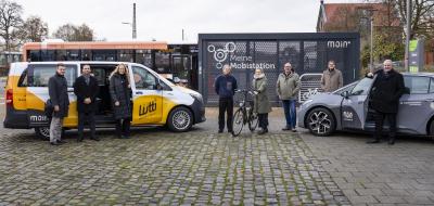 Eine Personengruppe steht vor einem Kleinbus und einem PKW.