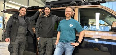 Drei Personen stehen vor einem Wohnmobil in einer Werkhalle.