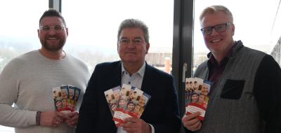 Drei Personen Stehen im Gegenlicht vor einer Glasfassade.