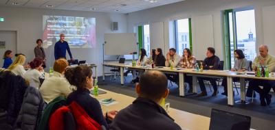 Seminarraum mit einer Personengruppe, die einem Referenten zuhört.