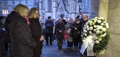 Personen stehen vor einem Gedenkranz.