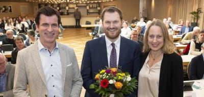 Drei Personen stehen in einem Sitzungssaal.