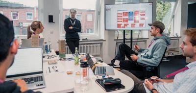 Vier Personen sitzen um einen Besprechungstisch herum, eine steht.