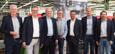 Sieben Personen stehen in einer Werkhalle.