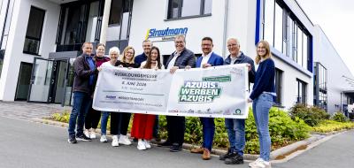 Personengruppe mit einem Banner steht vor einem Bürogebäude