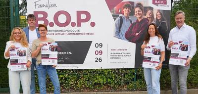 Fünf Personen stehen vor einem Zaun, an dem ein Plakat befestigt ist.