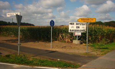 Radweg mit Verkehrsschildern vor einem Maisfeld