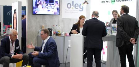 Mehrere Personen stehen an einem Messestand und sprechen miteinander.