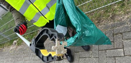 Eine Person mit einer Weste hält eine Abfalltüte und eine Müllzange in den Händen.