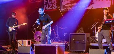 Drei Rockmusiker stehen auf einer Bühne.