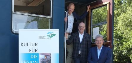 Drei Personen stehen am Einstieg eines Eisenbahnwaggons.