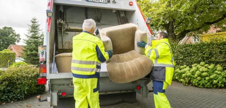 Zwei Personen entsorgen einen Sessel in einem Müllfahrzeug.