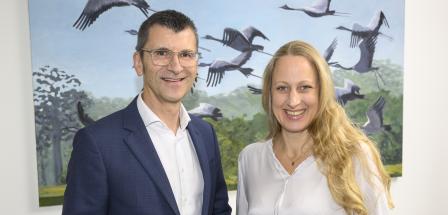 Zwei Personen stehen nebeneinander im Hintergrund ein Bild mit Vögeln.