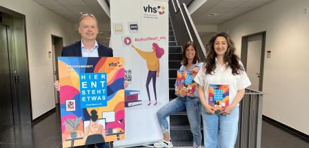 Drei Personen und ein Roll-Up-Poster stehen in einem Flur.