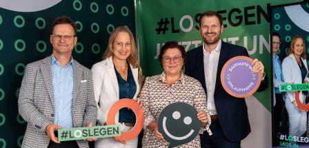 Vier Personen stehen vor einer Fotowand.