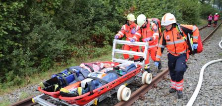 Drei Personen von Rettungsdiensten schieben eine Trage auf einer Schiene.