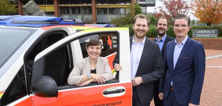 Vier Personen stehen an einem Blaulicht-Fahrzeug.