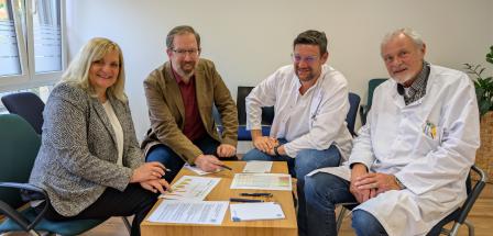 Vier Personen sitzen in einem Raum.