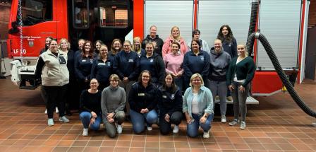 Eine Personengruppe steht vor einem Feuerwehrauto.