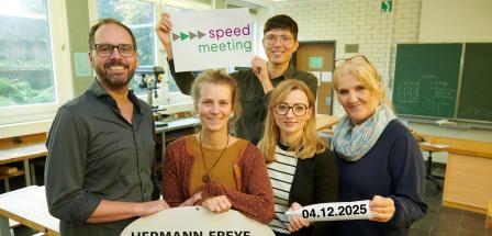 Fünf Personen stehen in einem Klassenraum.