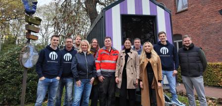 Personengruppe vor einem kleinen Holzhaus