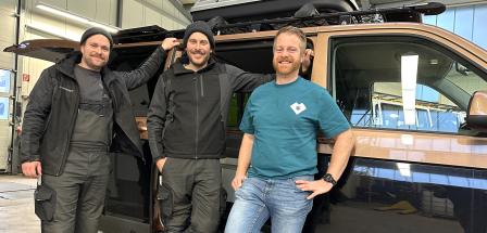 Drei Personen stehen vor einem Wohnmobil in einer Werkhalle.