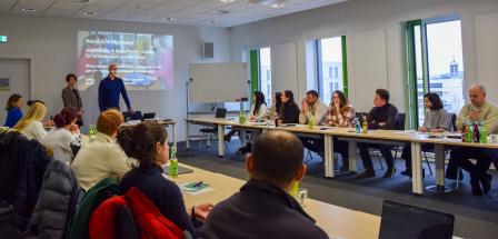 Seminarraum mit einer Personengruppe, die einem Referenten zuhört.