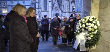 Personen stehen vor einem Gedenkranz.