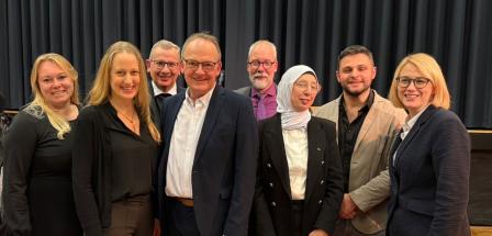 Eine Personengruppe steht vor einem Vorhang.