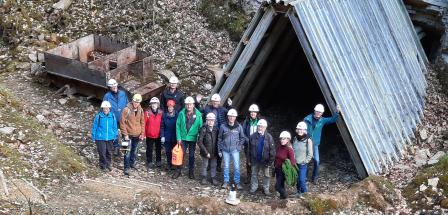 Personengruppe mit Helmen steht am Eingang zu einem Stollen.