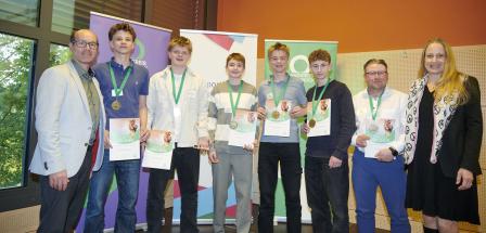 Personengruppe mit Medaillen und Urkunden steht vor Rollup Postern