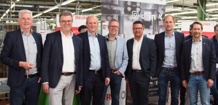 Sieben Personen stehen in einer Werkhalle.