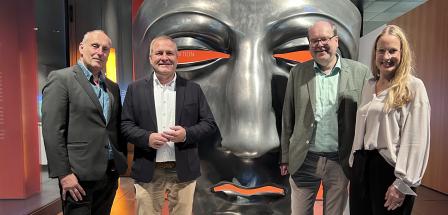Vier Personen vor einer übergroßen römischen Maske