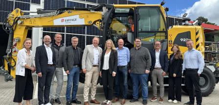 Personengruppe vor einem Bagger auf einem Hof