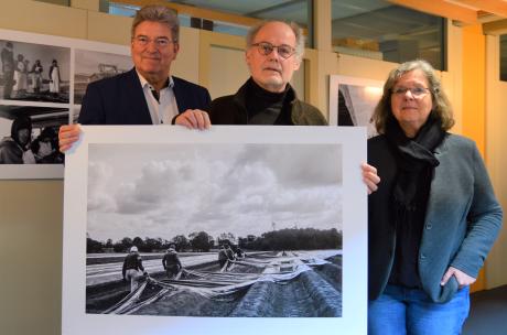 Drei Personen stehen in einem Flur und halten ein großformatiges Schwarz-weiß-Foto in den Händen.