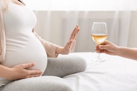 Eine schwangere Person weist ein Glas mit Weißwein zurück.