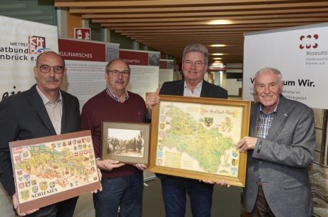 Ausstellung Kreishaus Heimatbund Vier Personen stehen vor den Postern einer Ausstellung und halten historische Karten in den Händen.