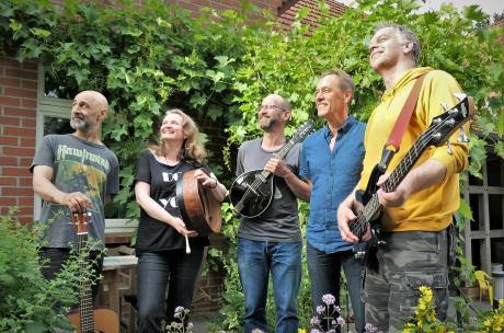Fünf Personen mit Musikinstrumenten stehen vor einem Haus.