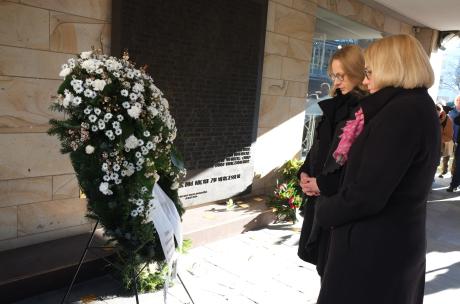 Zwei Personen stehen an einer Gedenkstätte vor einem Kranz.