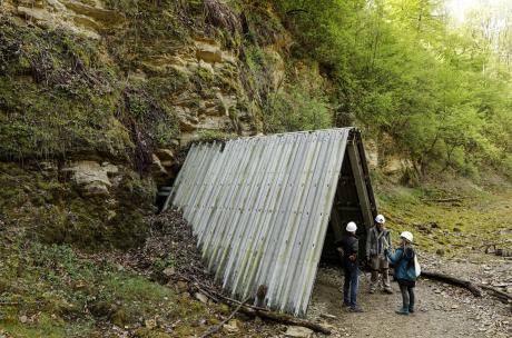 Drei Personen mit Helm stehen vor einem Stolleneingang.