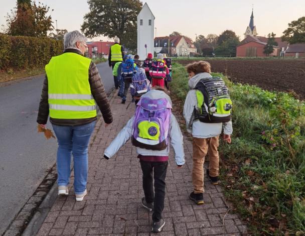 Eine Personengruppe geht auf einem Fußweg eine Straße entlang.