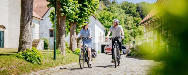 Zwei Personen auf Fahrrädern auf einer Dorfstraße.