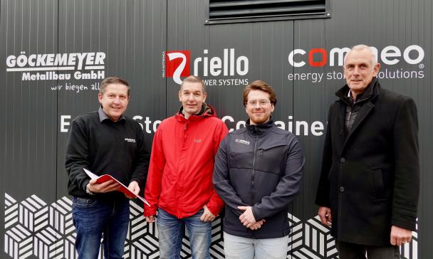 Vier Personen stehen vor einem grauen Metallcontainer.