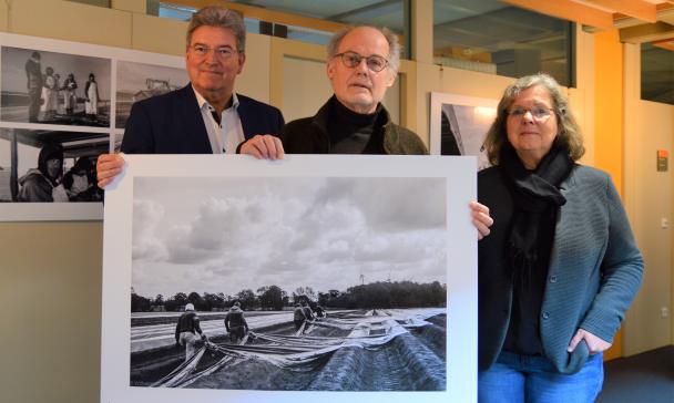 Drei Personen stehen in einem Flur und halten ein großformatiges Schwarz-weiß-Foto in den Händen.