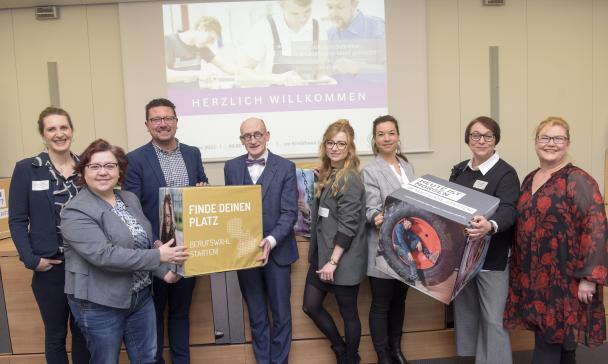 Eine Personengruppe mit bedruckten Schaumstoffwürfeln in den Händen steht vor einer Video-Projektionsfläche.
