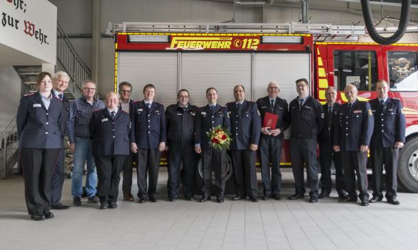 Eine Personengruppe in dunkelblauen Uniformen steht vor einem Feuerwehrfahrzeug.