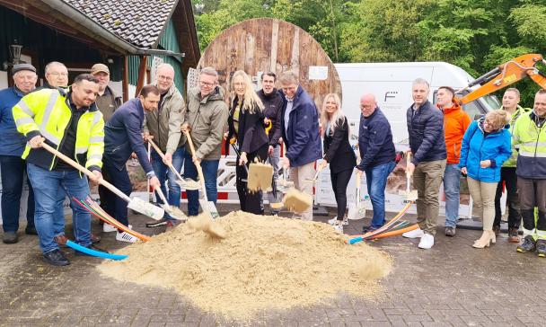 Eine Personengruppe mit Spaten steht hinter einem Sandhaufen.