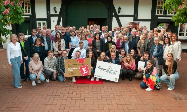 Eine große Personengruppe steht und hockt vor einem Fachwerkhaus.